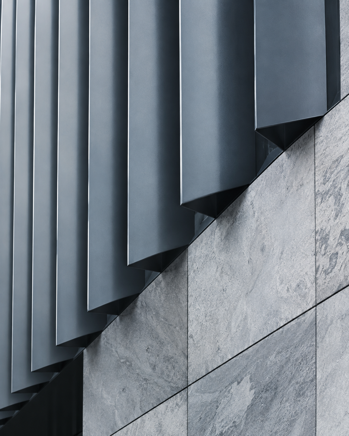 A study in structure: folded slate-blue architectural fins and cool stone in natural daylight.